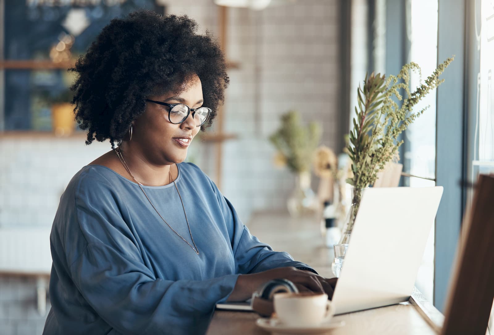 woman sitting at laptop at a cafe while drinking coffee