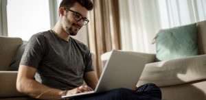 man with glasses sitting at computer and working on couch