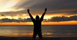 man in silhouette at beach with arms in air