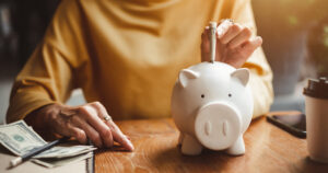 A senior citizen putting money in a piggy bank.