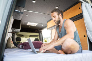 young bearded man with a laptop inside his camper van