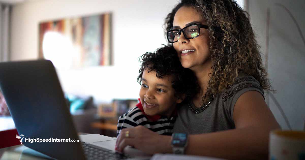 woman sitting at desk with son using computer in a dimly lit room