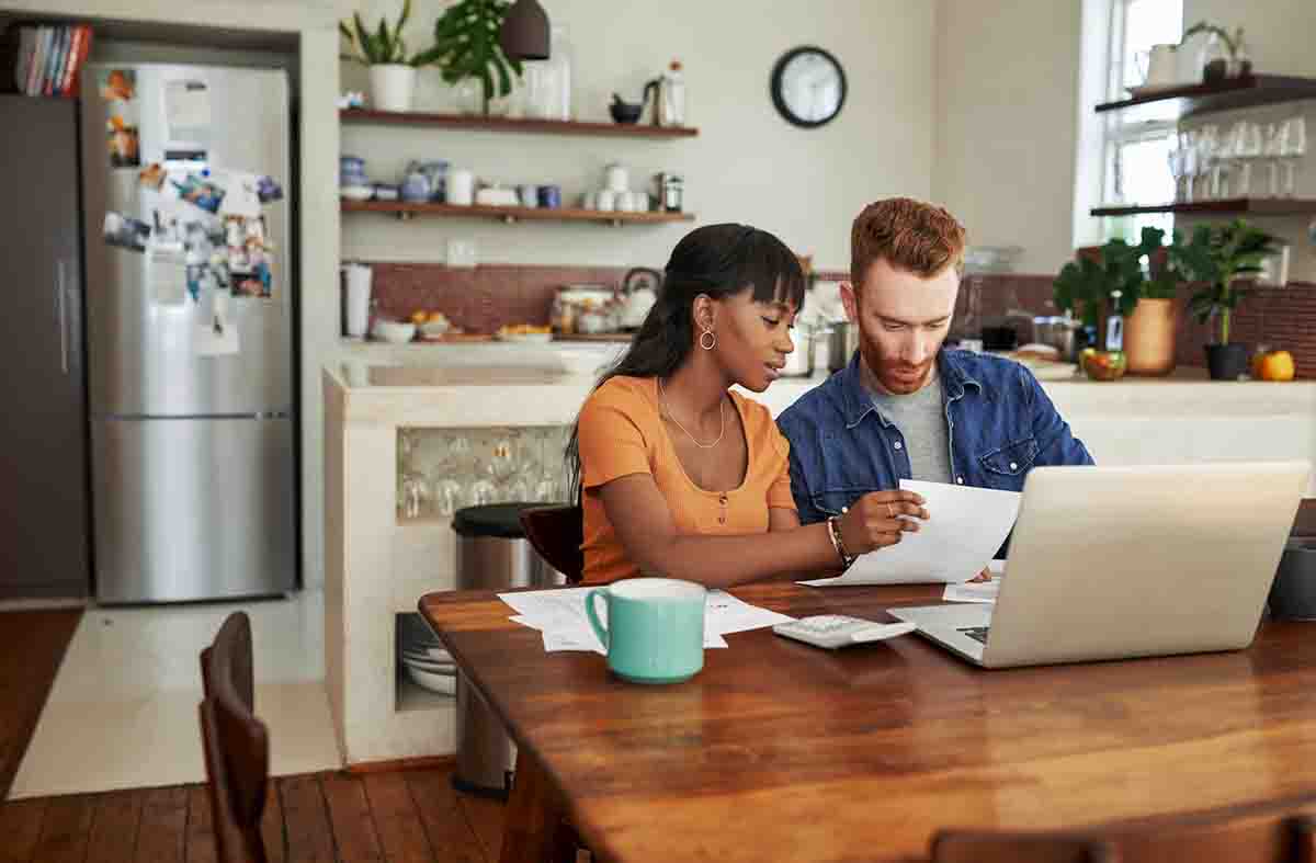couple sitting at table in kitchen using laptop