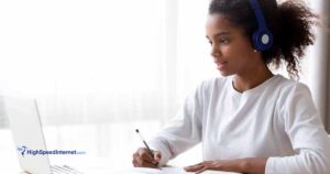 african american student working at desk with lots of natural light and wearing headphones.