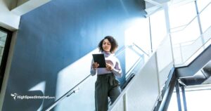 woman walking down a brightly lit stairway in an office building using an ipad