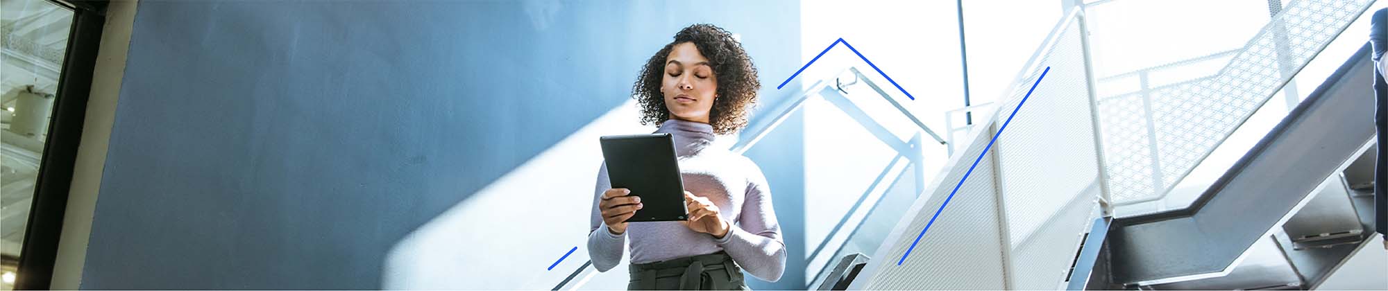 woman walking down a brightly lit stairway in an office building using an ipad