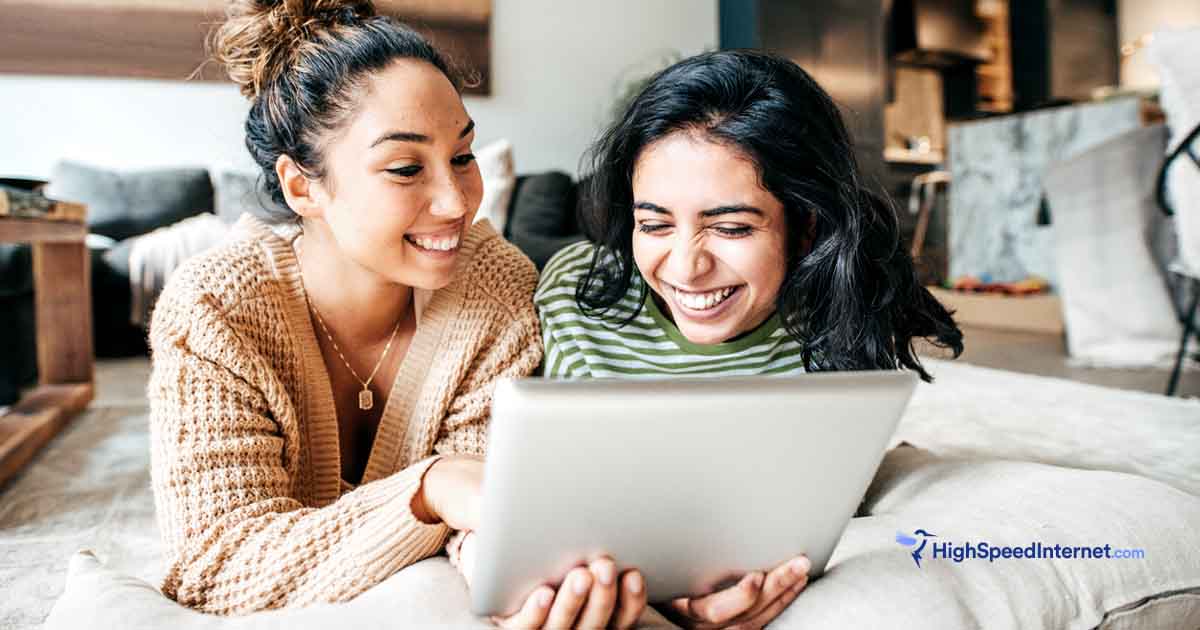 Two women laying down using ipad in a cozy room