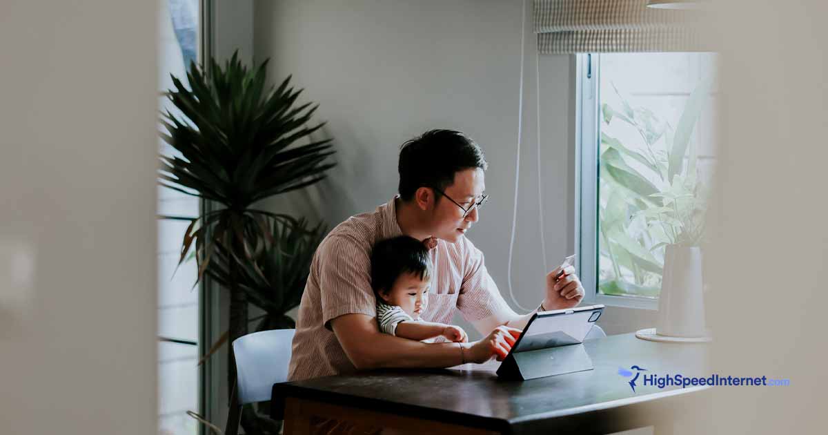 Father sitting at kitchen table with daughter on his lap using an ipad