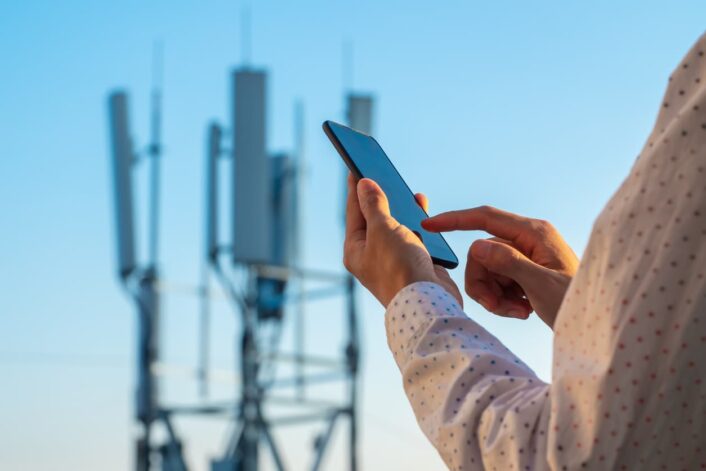 person holding a cell phone while standing near a cellular tower