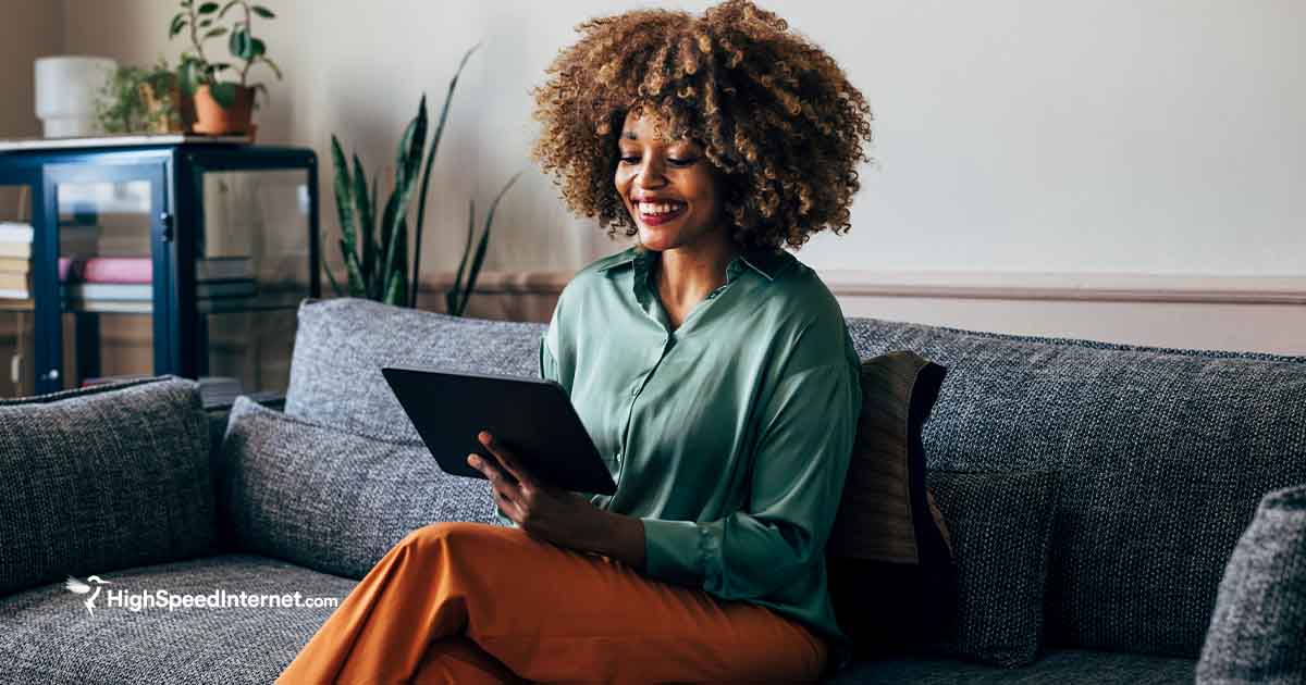 Woman on a sofa using a tablet to access the internet and smiling