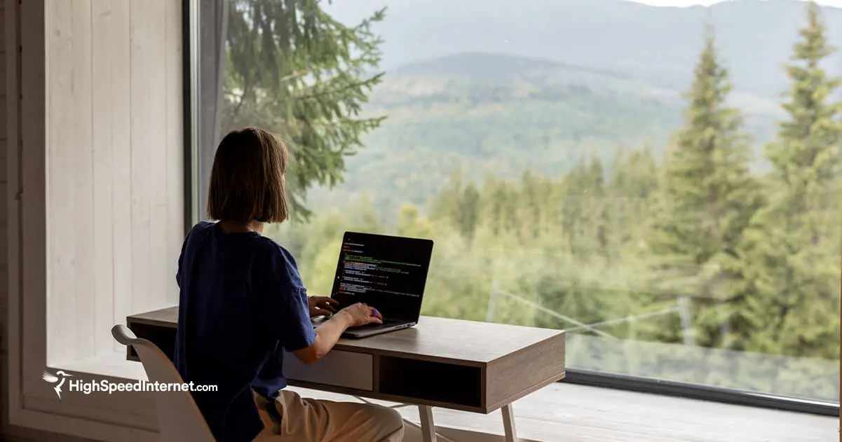 Woman typing on laptop near a window with a view of mountains