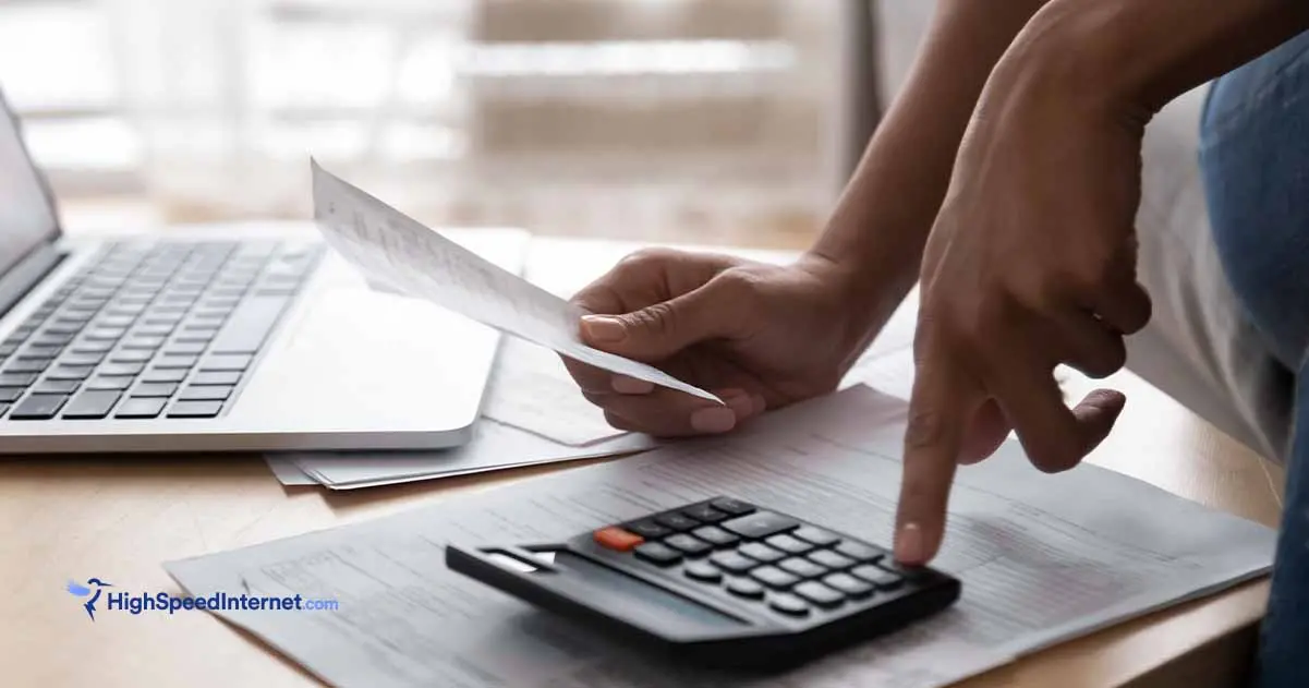 Hands pressing a button on a calculator with a laptop in the background